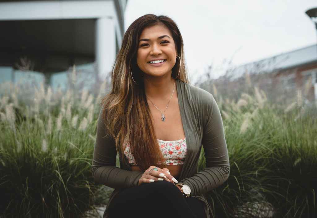 smiling woman wearing gray cardigan seating in front of dandelions